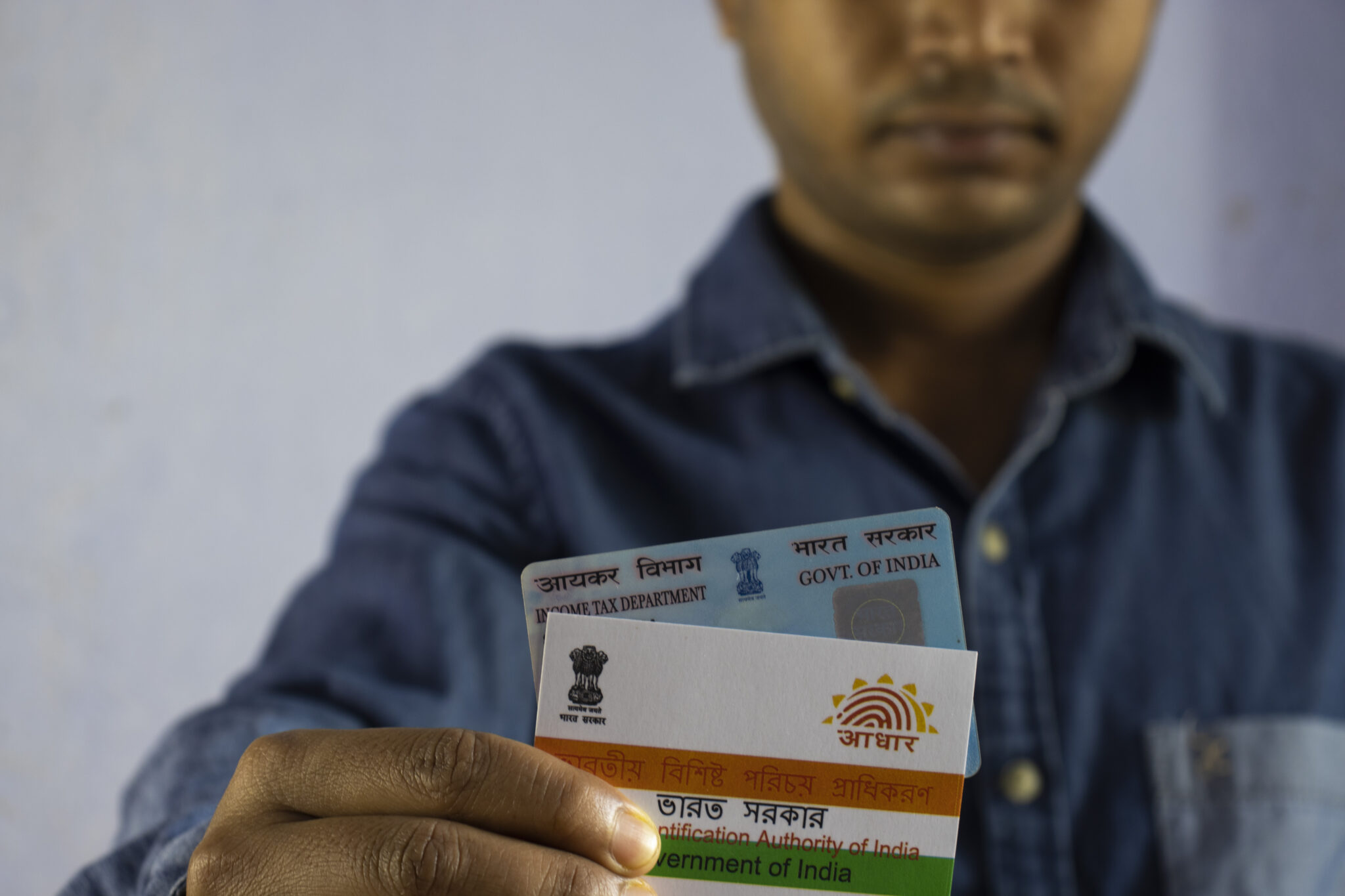 an Indian man holding PAN and aadhaar cards on white background with selective focus or shallow depth of field