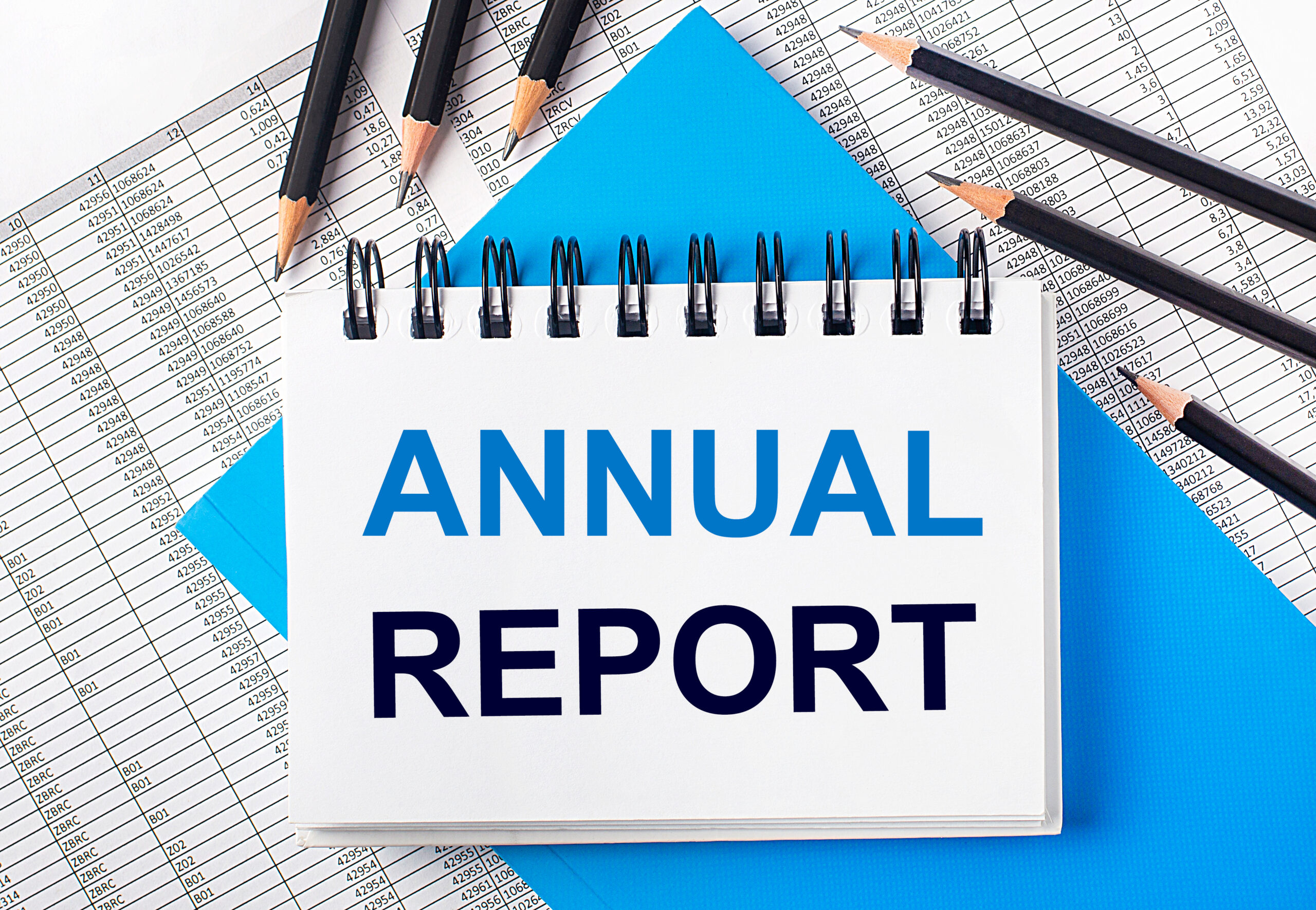 White notebook with the text ANNUAL REPORT on the table next to black pencils on a blue background and reports. Business concept